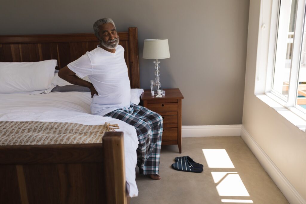 Front view of a senior African American man suffering from back pain in bedroom at home