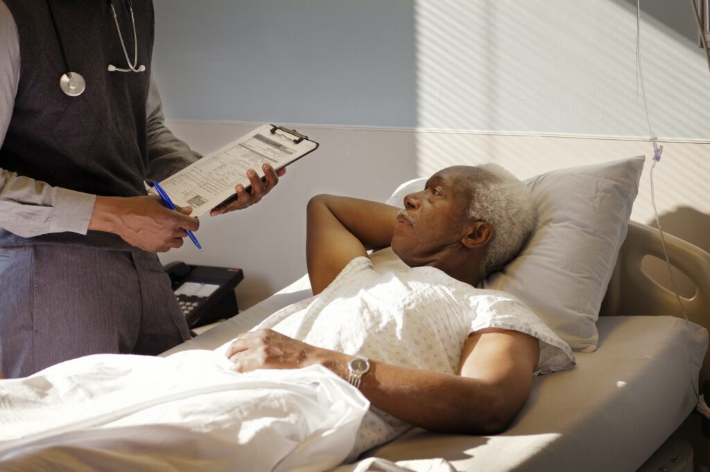 Senior Man Looking At Doctor While Lying On Bed In Hospital
